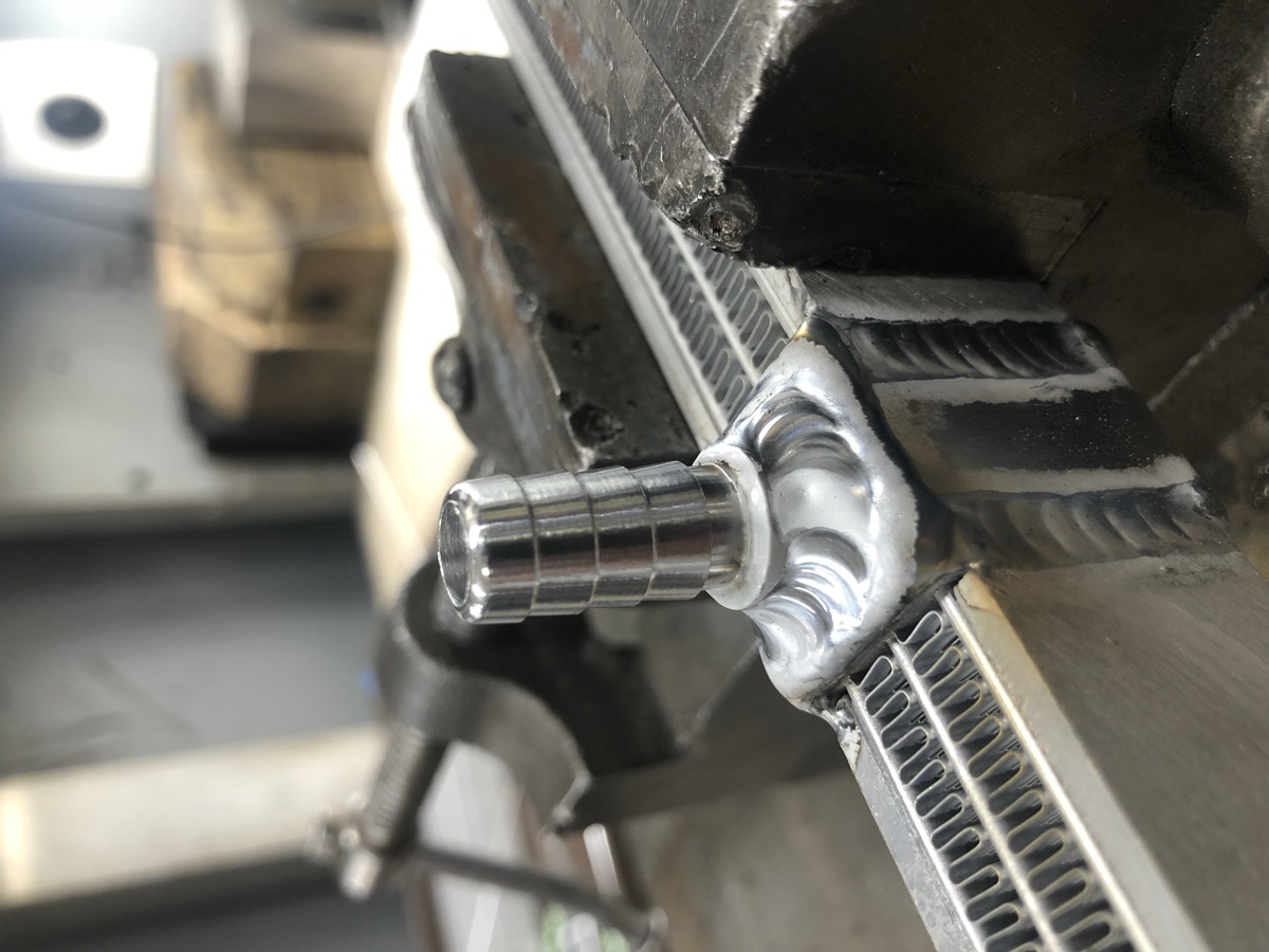 Machined barb fitting welded onto an aluminum radiator held in a vise